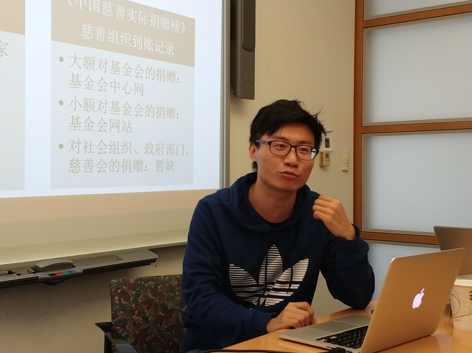 講座現場照片：一位戴眼鏡的男士坐在筆電前發言；身後投影幕是「《中國慈善實際捐贈榜》慈善組織到賬記錄」簡報，列出大額、小額對基金會捐贈與對社會組織捐贈三條要點。